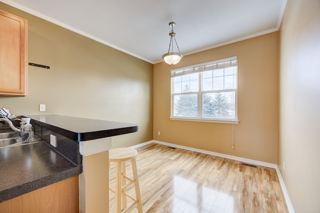 kitchen featuring pendant lighting, light hardwood / wood-style floors, a breakfast bar area, light brown cabinetry, and ornamental molding