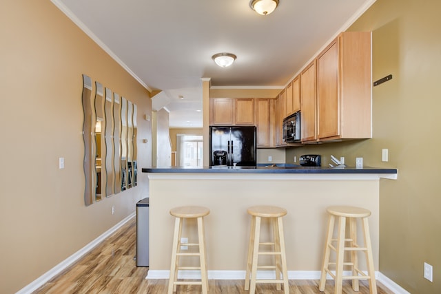 kitchen featuring kitchen peninsula, light brown cabinetry, a kitchen breakfast bar, crown molding, and black appliances