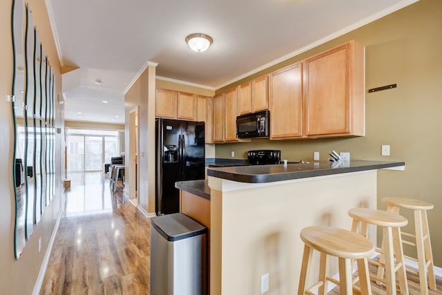 kitchen with kitchen peninsula, a breakfast bar, black appliances, and light brown cabinets