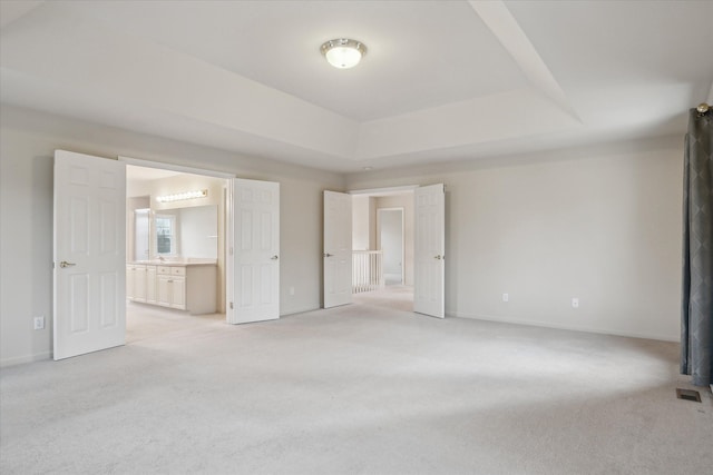 unfurnished bedroom featuring light carpet, a raised ceiling, and ensuite bath