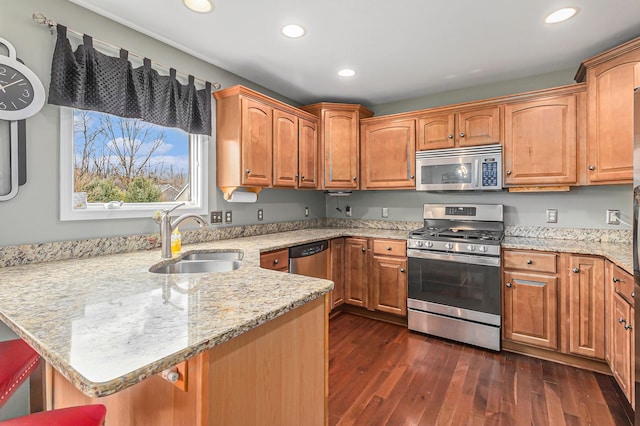 kitchen with dark wood-type flooring, sink, kitchen peninsula, stainless steel appliances, and light stone countertops