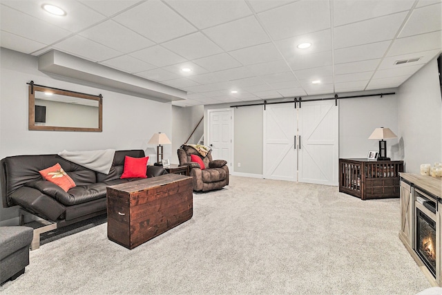 living room featuring a barn door, light colored carpet, and a drop ceiling