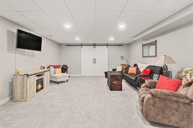 carpeted living room featuring a barn door and a drop ceiling