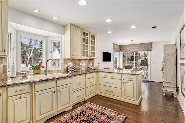 kitchen featuring dark hardwood / wood-style floors, kitchen peninsula, sink, cream cabinetry, and stone countertops