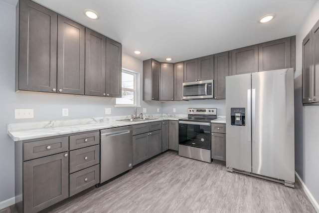 kitchen featuring light stone countertops, sink, light wood-type flooring, and appliances with stainless steel finishes