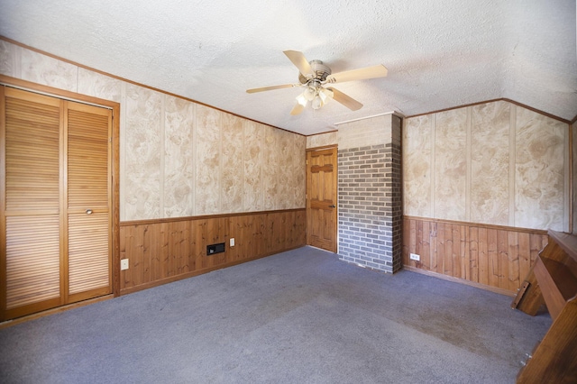 carpeted spare room with a textured ceiling, ceiling fan, ornamental molding, and wood walls