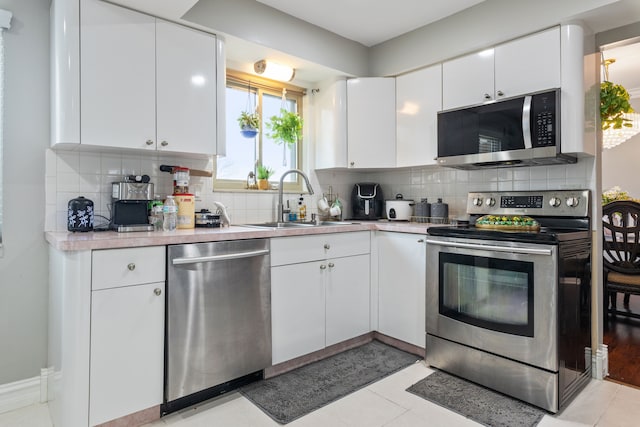 kitchen featuring backsplash, sink, light tile patterned floors, appliances with stainless steel finishes, and white cabinetry