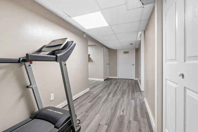 exercise area featuring a drop ceiling and light wood-type flooring