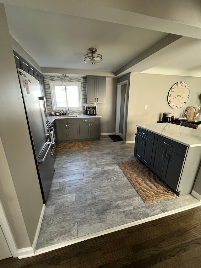 kitchen featuring gray cabinetry, a sink, wood finished floors, light countertops, and baseboards