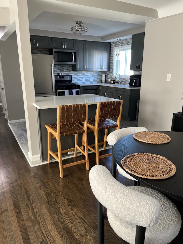 kitchen with a breakfast bar area, stainless steel appliances, backsplash, dark hardwood / wood-style flooring, and sink