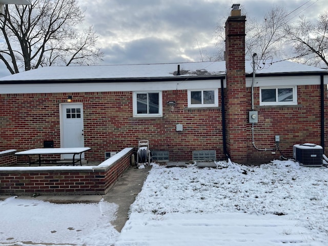 snow covered back of property featuring central AC unit