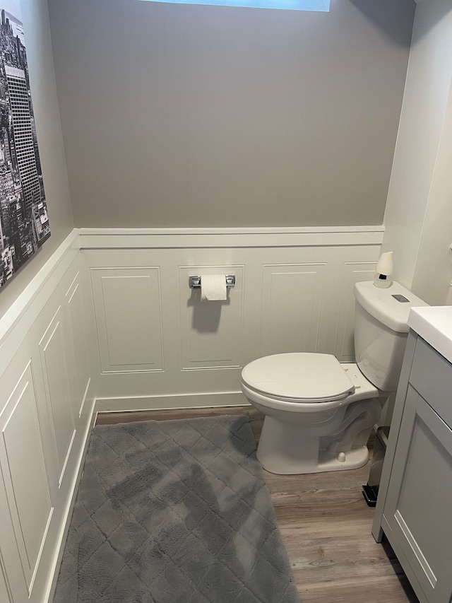 bathroom with vanity, toilet, wood finished floors, and wainscoting