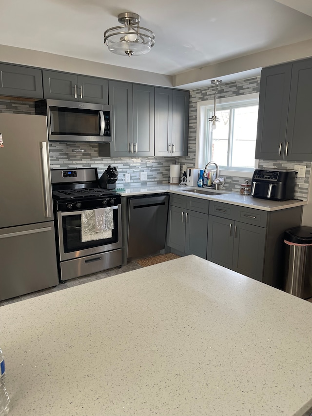 kitchen with tasteful backsplash, sink, hanging light fixtures, appliances with stainless steel finishes, and gray cabinetry