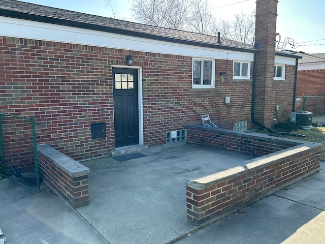 back of property with brick siding, central air condition unit, a shingled roof, and a patio