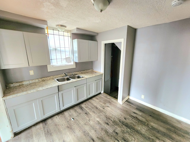 kitchen featuring white cabinets, sink, a textured ceiling, and light hardwood / wood-style flooring