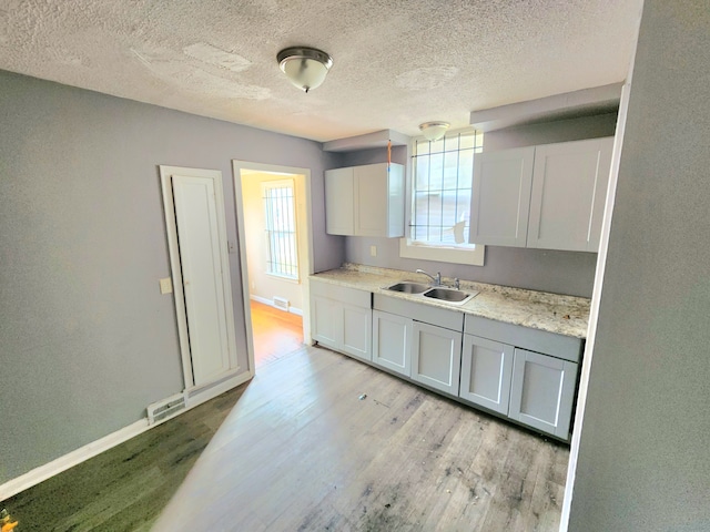 kitchen featuring light stone countertops, a textured ceiling, white cabinets, light hardwood / wood-style floors, and sink