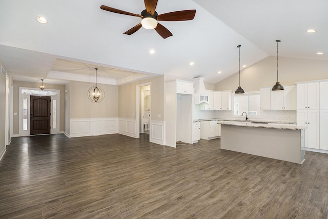 kitchen with light stone counters, ceiling fan, white cabinetry, hanging light fixtures, and an island with sink