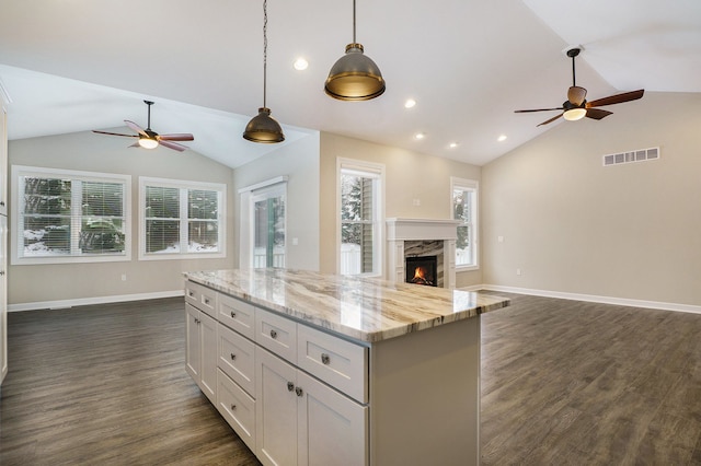 kitchen featuring a high end fireplace, light stone counters, vaulted ceiling, decorative light fixtures, and white cabinetry