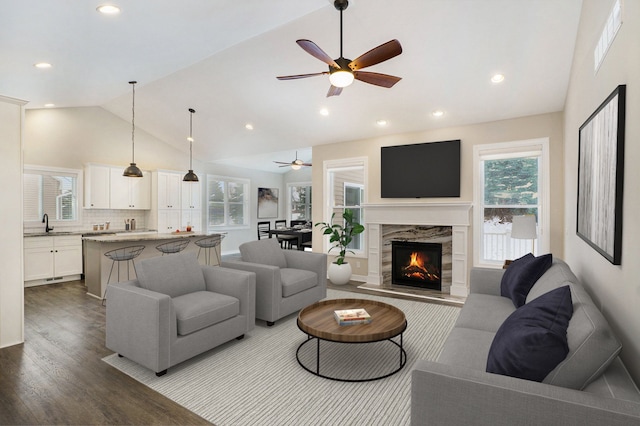 living room featuring ceiling fan, sink, light hardwood / wood-style flooring, lofted ceiling, and a fireplace