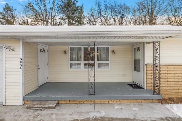 snow covered property entrance featuring covered porch and a carport