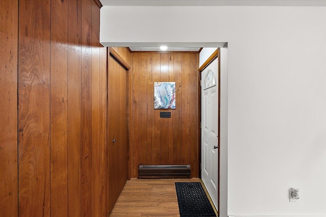 doorway with a baseboard heating unit, wooden walls, and light hardwood / wood-style floors