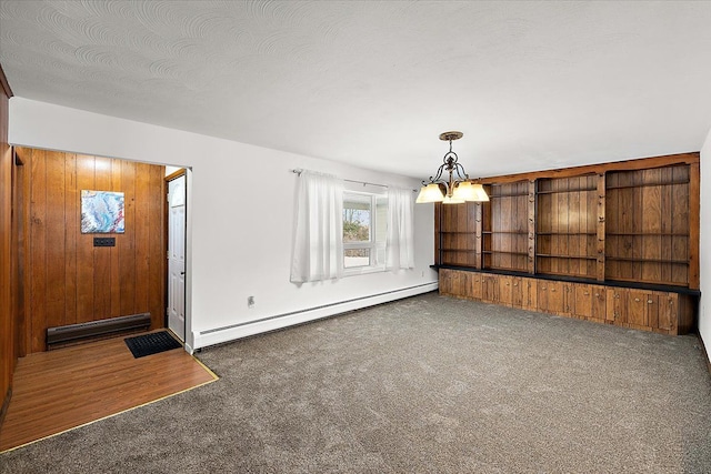 entrance foyer featuring an inviting chandelier, wooden walls, a baseboard radiator, and dark colored carpet