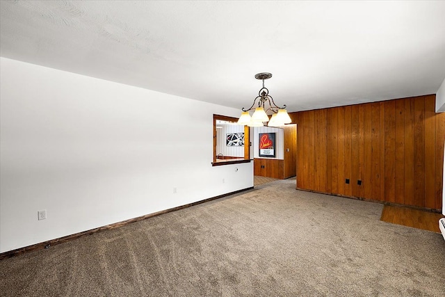 spare room featuring a notable chandelier, wooden walls, and carpet