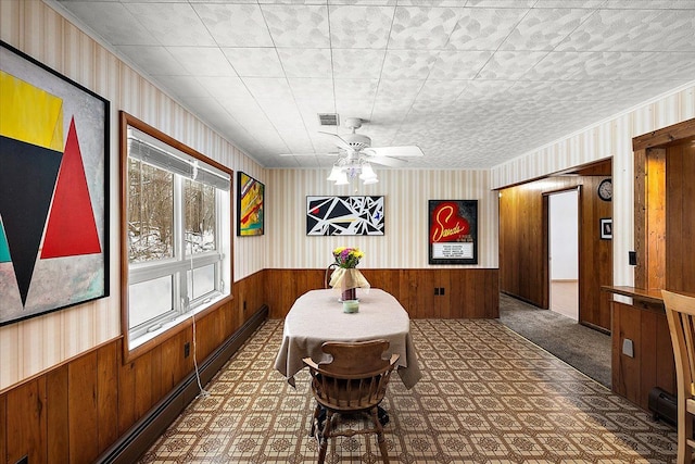 dining space featuring dark carpet, wood walls, ceiling fan, and baseboard heating