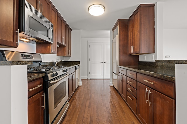 kitchen with stainless steel appliances, dark stone counters, and dark hardwood / wood-style floors