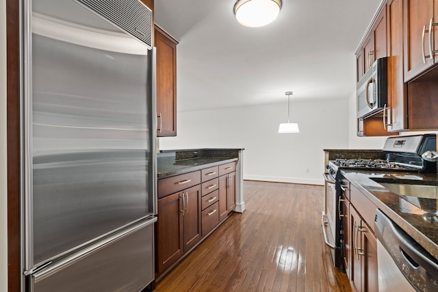 kitchen featuring sink, dark stone countertops, dark hardwood / wood-style flooring, pendant lighting, and appliances with stainless steel finishes