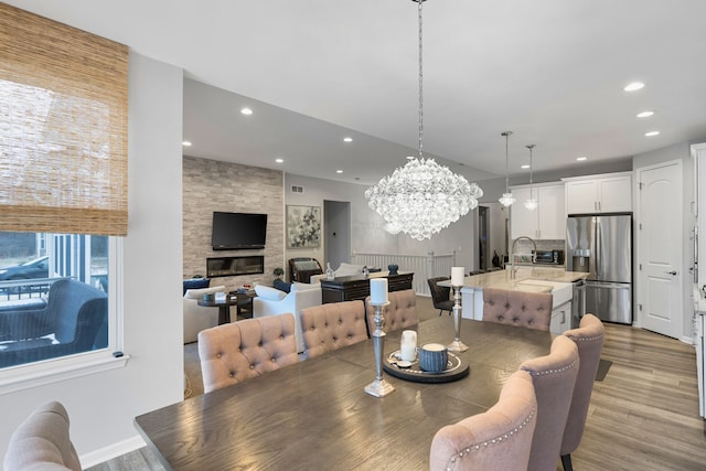 dining space with a notable chandelier, a stone fireplace, and light hardwood / wood-style flooring