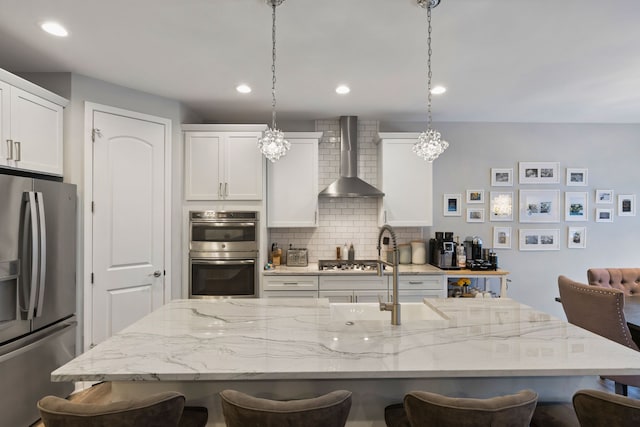 kitchen featuring a kitchen bar, wall chimney exhaust hood, stainless steel appliances, and decorative light fixtures