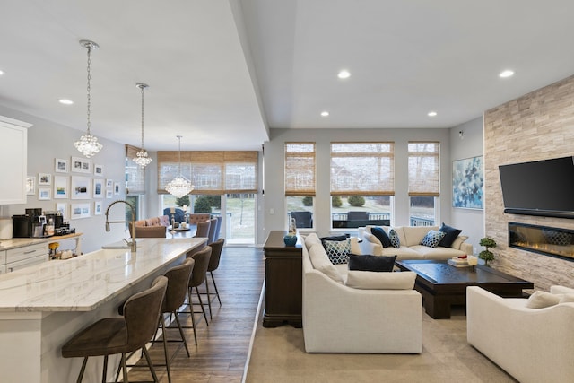 living room with light hardwood / wood-style flooring, a stone fireplace, and a notable chandelier