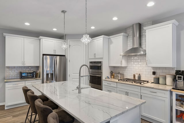 kitchen with sink, stainless steel appliances, white cabinetry, and wall chimney range hood