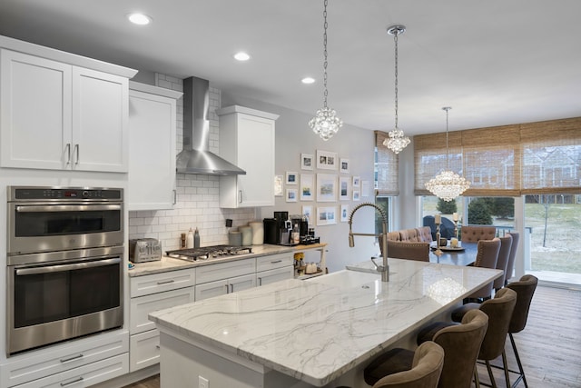 kitchen with white cabinetry, stainless steel appliances, wall chimney range hood, and an inviting chandelier