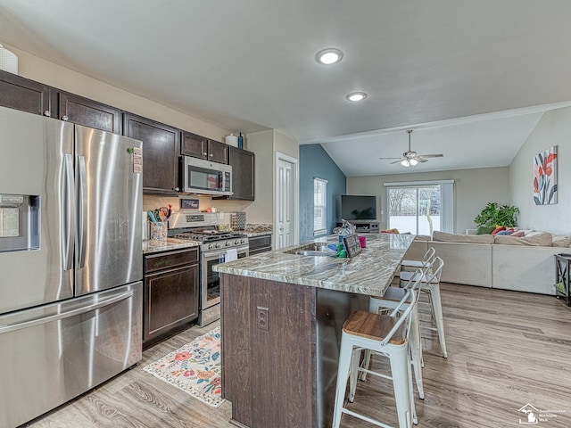 kitchen featuring sink, dark brown cabinets, a breakfast bar, a center island with sink, and appliances with stainless steel finishes