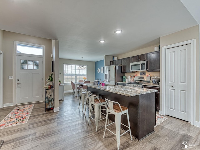 kitchen with appliances with stainless steel finishes, a kitchen breakfast bar, dark brown cabinetry, a kitchen island with sink, and light hardwood / wood-style flooring