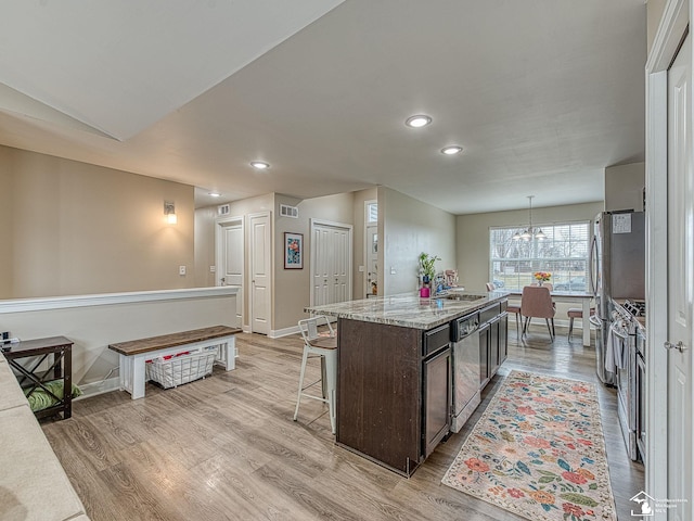 kitchen with decorative light fixtures, a kitchen island, light wood-type flooring, and dark brown cabinetry