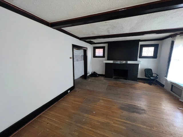 unfurnished living room featuring a large fireplace, dark hardwood / wood-style floors, beam ceiling, and a textured ceiling