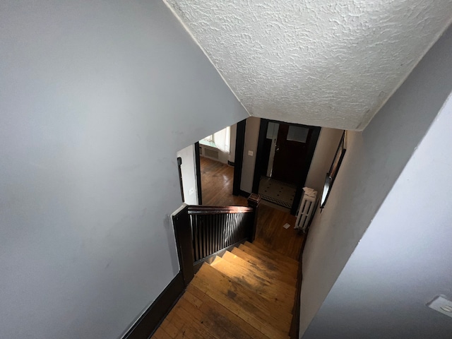 stairway featuring wood-type flooring, a textured ceiling, and vaulted ceiling