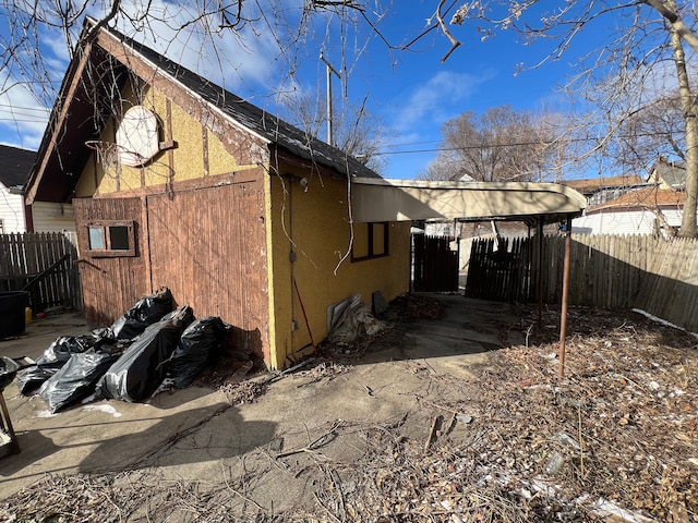 view of property exterior featuring stucco siding, a carport, and fence