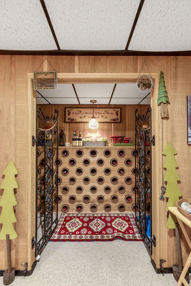 wine room featuring wood walls, a drop ceiling, and carpet