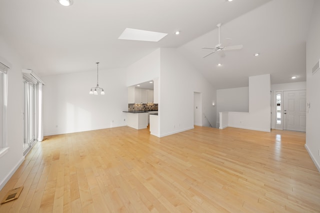 unfurnished living room featuring ceiling fan with notable chandelier, light hardwood / wood-style flooring, and vaulted ceiling with skylight