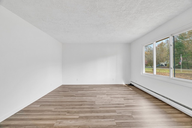 empty room with a textured ceiling, light wood-type flooring, and baseboard heating