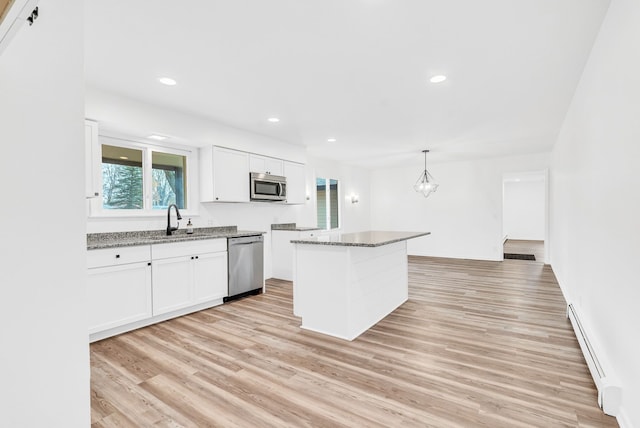 kitchen with appliances with stainless steel finishes, sink, a baseboard radiator, white cabinetry, and hanging light fixtures