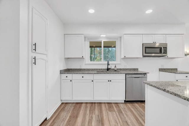 kitchen with white cabinets, sink, light hardwood / wood-style floors, light stone counters, and stainless steel appliances