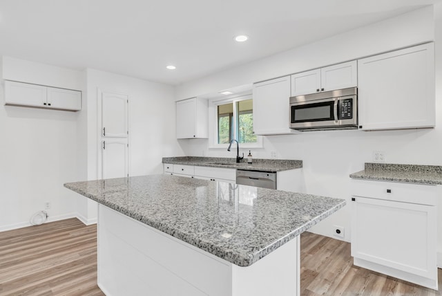 kitchen with light stone counters, stainless steel appliances, sink, white cabinets, and a kitchen island