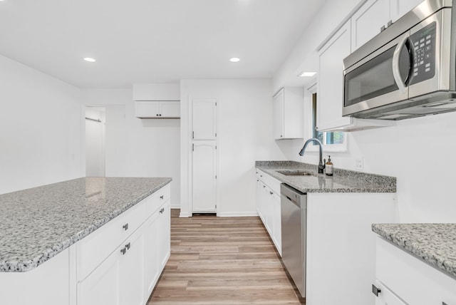 kitchen with light stone countertops, stainless steel appliances, sink, light hardwood / wood-style flooring, and white cabinets