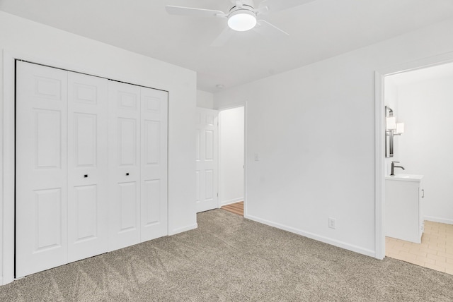 unfurnished bedroom with a closet, light colored carpet, ceiling fan, and connected bathroom