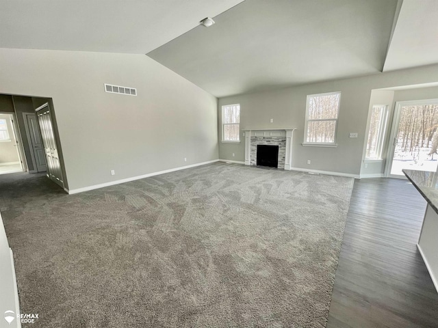 unfurnished living room with lofted ceiling, a stone fireplace, and dark carpet